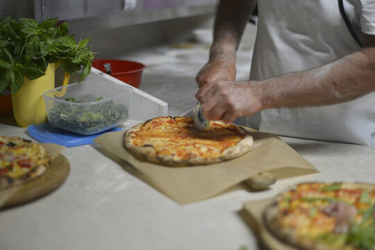 pizzaiolo taglia la pizza prima di servirla al cliente della pizzeria