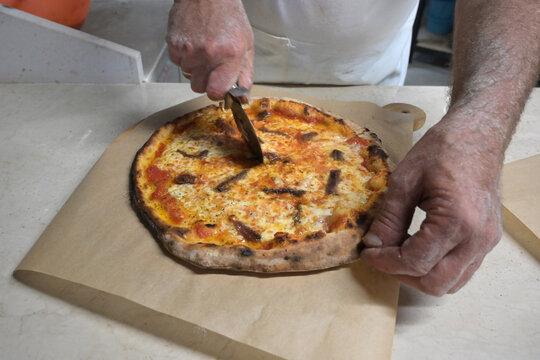 pizzaiolo taglia la pizza prima di servirla al cliente della pizzeria