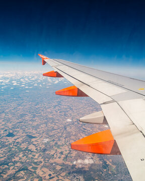 An aerial view from an airplane window captures the wing of an easyJet aircraft soaring above a patchwork of farmlands and scattered clouds, representing the perspective of a passenger during a flight