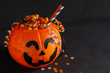 Naklejka premium Halloween celebration and trick or treat tradition, plastic pumpkin bucket filled with candy corn and party decorations on a dark background