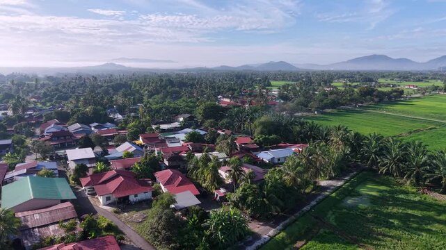 An expansive aerial view captures a rural Kubang Semang village surrounded by lush farmland, vibrant greenery, and mountain landscapes