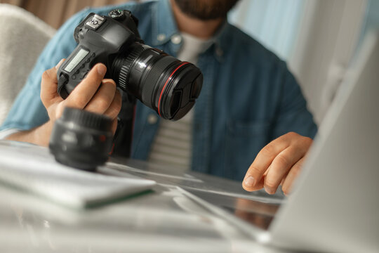 Close up photographer holding digital camera while using laptop