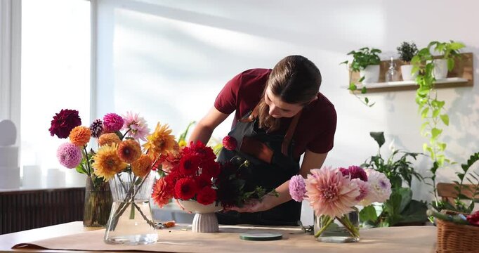 Florist making bouquet of beautiful dahlia flowers at table in shop