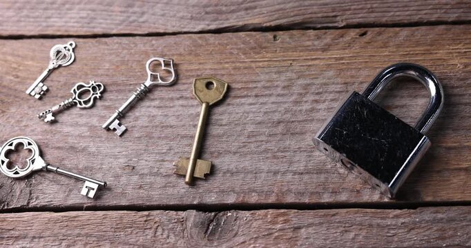 Different metal keys and lock on wooden background, closeup. Camera moving right
