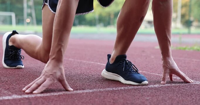 Athletic man in starting position for run at stadium, closeup. Camera moving down