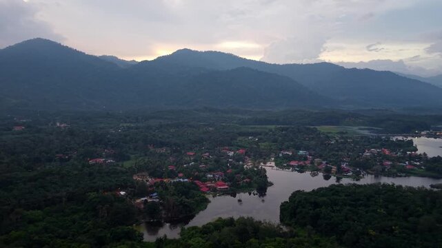 Clouds loom over distant mountains. Villages nestle beside calm, wide waters at Tasik Raban