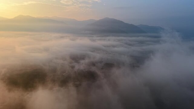 Golden hour light glows over mountain peaks. Fog swirls through valleys like soft white waves at Tasik Raban