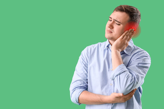 Earache and hearing loss concept, young man suffering from ear pain with red inflammation zone on a green background