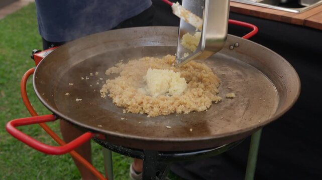 Chef adding and stirring minced garlic into a spanish paella pan