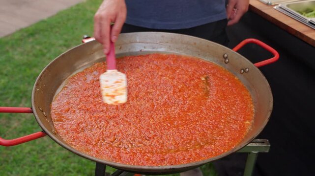 Chef cooking spanish paella tomato sofrito sauce outdoors