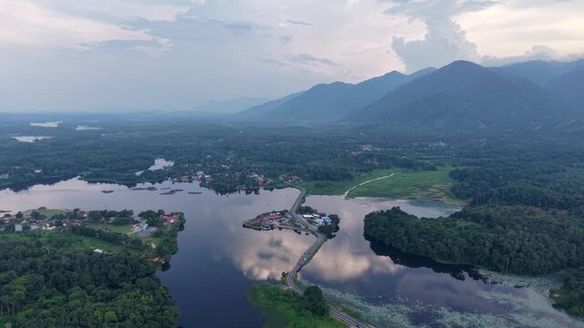 Aerial landscape showing a winding river surrounded by dense forest and mountainous terrain under a cloudy sky during dusk at Tasik Raban