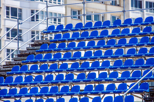 Empty blue seats on a temporary metal grandstand under a sunny sky. Removable bleachers for outdoor sports, concerts, and public events.