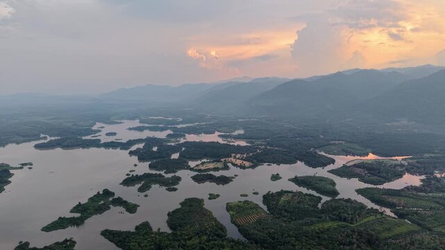 Aerial landscape showing numerous small islands covered in trees surrounded by calm lake water, with mountain ranges and dramatic sky during sunset in the background at Tasik Raban