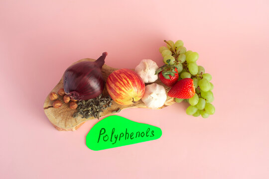 Products containing beneficial polyphenols. Grapes, onions, garlic, chocolate, tea &mdash; close‑up on a light background, and the text &ldquo;polyphenols&rdquo; written on paper.