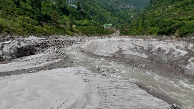 High angle drone tracking shot over extensive silt deposits and eroded banks along the Parvati River basin, documenting severe flood destruction in Himachal Pradesh, India.