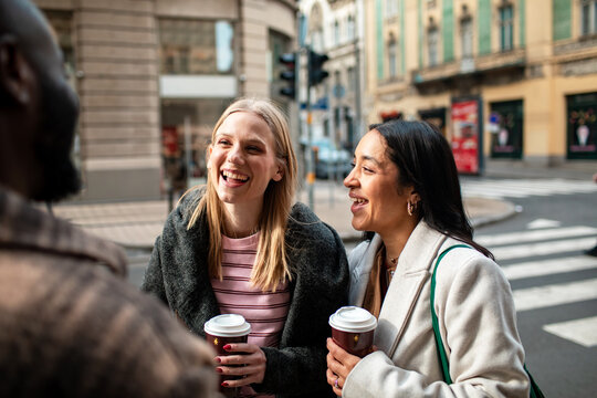 Friends laughing with takeaway coffee on city street corner