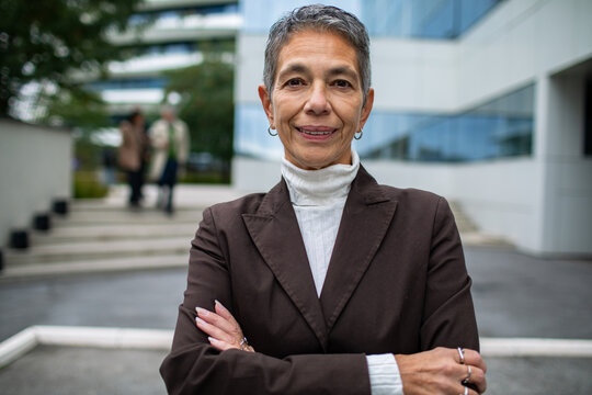 Confident senior businesswoman with crossed arms outside modern office