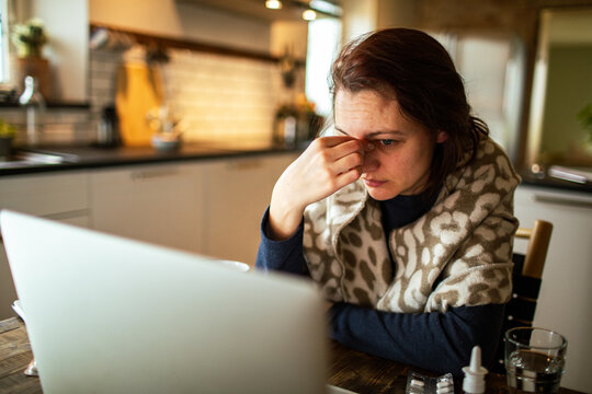 Sick woman with headache using laptop in home kitchen