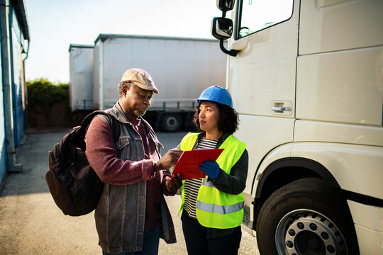 Logistics worker and truck driver reviewing paperwork at loading dock
