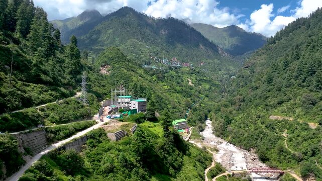 Aerial shot over the colorful tin roofs and lush agricultural terraces of Barshaini village, a vibrant trekking basecamp in the Parvati Valley of Himachal Pradesh, India.