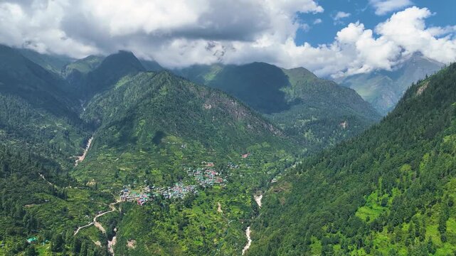 Aerial shot over the colorful tin roofs and lush agricultural terraces of Barshaini village, a vibrant trekking basecamp in the Parvati Valley of Himachal Pradesh, India.