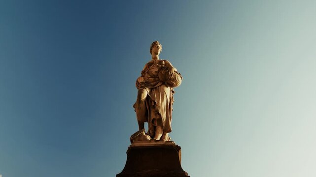 A ground-level arc around the plinth keeps a carved allegorical figure high in frame with a low cloud passing behind, in Florence, Italy.