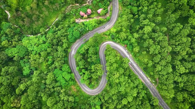 High angle drone glide over a winding mountain pass surrounded by vibrant summer canopy, an ideal commercial establishing shot for automotive advertising in India.