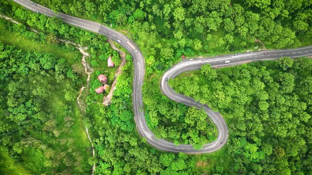Overhead drone sweep of a winding tarmac road navigating pristine green wilderness, highlighting off-grid overland travel and road trip escapism in Himachal Pradesh.