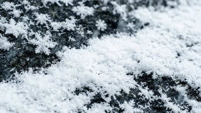 Real snowflakes falling and settling on dark stone ground