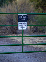 Green gate stands closed by a sign in English and Spanish languages. Sign urges users to keep gate shut. © missy_photos