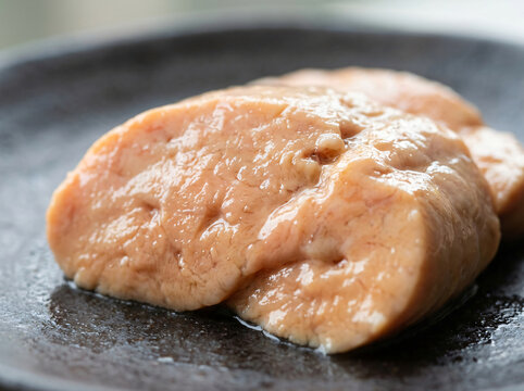 Fresh raw monkfish liver served on a dark ceramic plate.