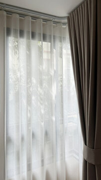 Luxury beige ripple fold curtains with white sheer on a curved track and sunlight