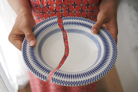 Person holds broken plate at home during day
