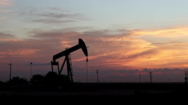 Pump Jack Pumping in Desert Field during Morning Sunrise with Dramatic Clouds
