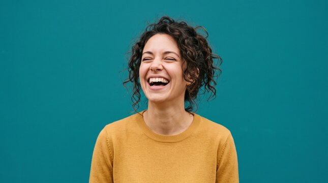 Portrait of a Joyful Young Woman Laughing Heartily Against a Solid Teal Background