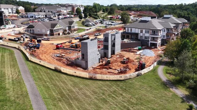Construction spreads across an apartment development in Lynchburg, Virginia, red earth, stacked materials and heavy equipment surrounding half finished buildings. Aerial wide shot