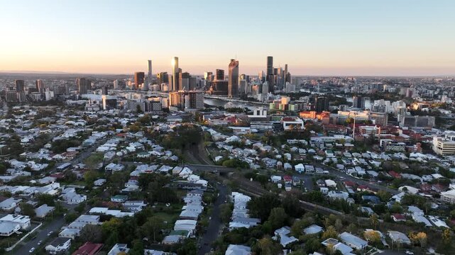 Slow aerial pan across Brisbane from above suburban streets at sunset, rotating to reveal the CBD skyline and river with the inner city spread across the horizon, St Lucia, Brisbane, Queensland.