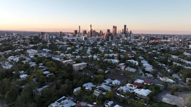 Static aerial establishing shot over St Lucia suburbs toward the Brisbane CBD skyline at sunset, residential rooftops and treetops below, St Lucia, Brisbane, Queensland, Australia.