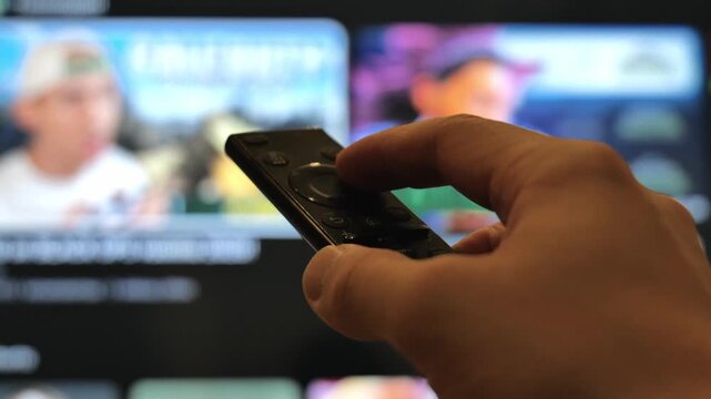 Close Up View of Male Hand Operating Infrared Remote in Front of TV