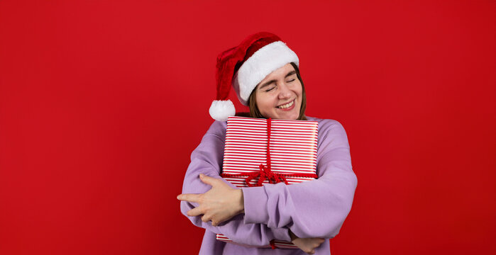 Christmas studio shot of a cheerful and happy woman with a gift box against red background. Copy space banner 