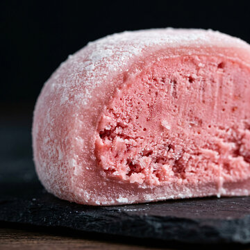 A close up view of a single pink strawberry mochi ice cream ball on a dark slate board.