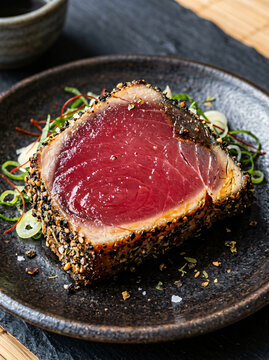 Seared Ahi Tuna Steak Crusted with Black Sesame Seeds Served on a Dark Plate.