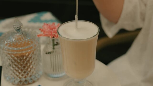 Stirring with a dessert spoon to make a latte. Latte in a beautiful coffee mug.