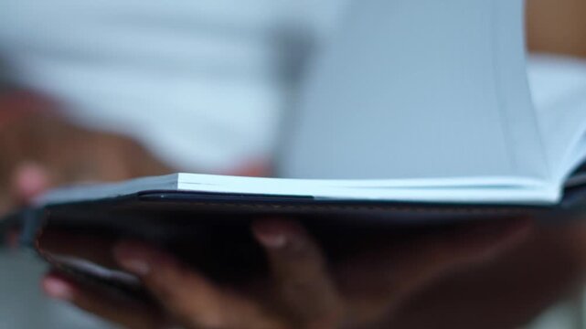 Close up of dark skinned hands leafing through the pages of a leather bound book or journal in search of information