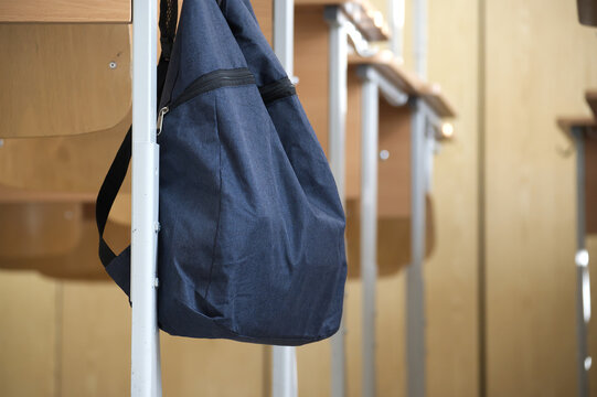 Dark Blue Backpack Hanging on Wooden School Desk in Empty Classroom During Study Break