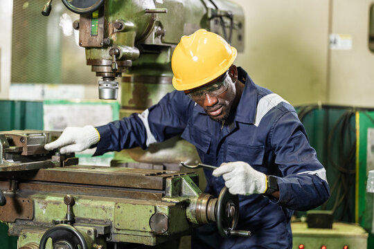 African adult man technician adjusts machine table while holding hooked tool, checking setup point during maintenance workflow, safe operation and precision support in industrial workshop.