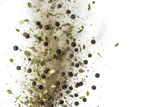 Dynamic explosion of black peppercorns and green herbs on transparent background for creative spice design