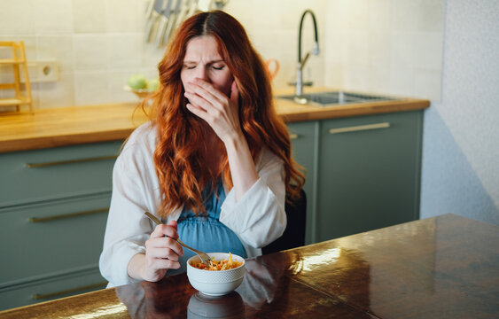 Pregnant woman experiencing nausea and food aversion while eating a meal at home, illustrating morning sickness and common pregnancy symptoms.