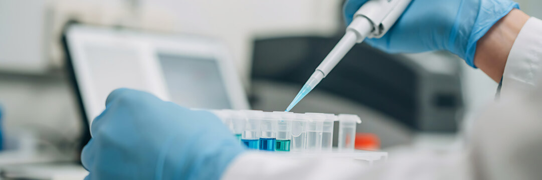 Scientist in blue latex gloves using a micropipette to transfer blue liquid into small plastic test tubes inside a laboratory setting