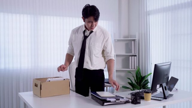 Young Asian man packing personal belongings into cardboard box after resigning from office job